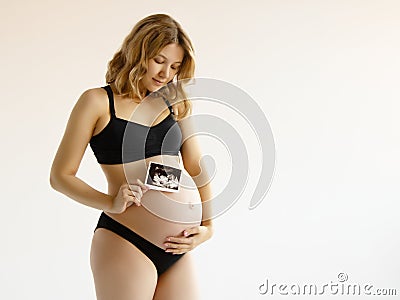 Prenatal ultrasound screening. Beauty pregnant holding sonogram picture of unborn baby inside her big belly Stock Photo