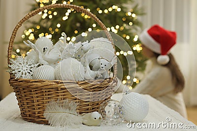 Preparation for Christmas. White Christmas ornaments in wicker basket. Girl with santa hat decorating Christmas tree. Stock Photo