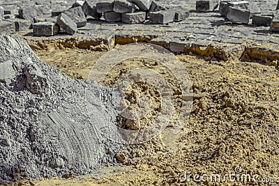 Preparation of dry cement-sand mixture on the background of disassembled granite pavers. Pile of gray dry cement in the middle of Stock Photo