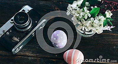 Preparation for Easter. Colorful handmade Easter eggs, paint, retro camera and vase with flowers on a wooden background Stock Photo