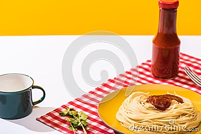 Prepared spaghetti with tomato sauce beside cup on white surface on yellow background Stock Photo