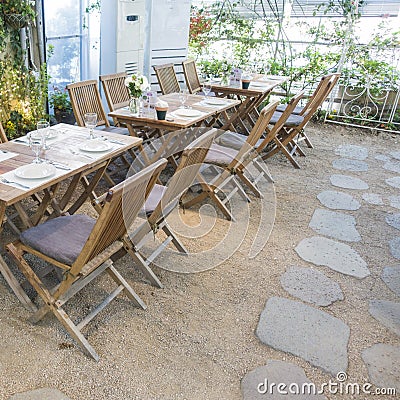 Prepared wooden tables and chairs with floral decorations and stone paved floor in indoor garden restaurant Stock Photo