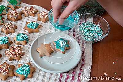 Preparing for Christmas, decorating traditional gingerbread with multicolored sugar glaze, the girl folds the cookies in a white Stock Photo