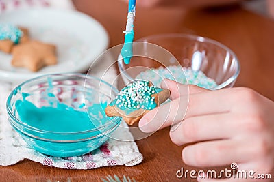 Preparing for Christmas, decorating traditional gingerbread with multicolored sugar glaze, the girl folds the cookies in a white Stock Photo