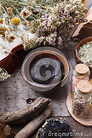 Preparing cosmetic black mud mask in ceramic bowl on vintage wooden background. Front view of facial clay emulsion on table with Stock Photo