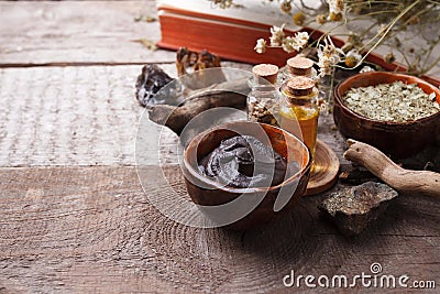 Preparing cosmetic black mud mask in ceramic bowl on vintage wooden background. Front view of facial clay emulsion on table Stock Photo