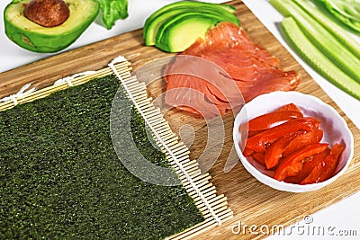 Preparing homemade sushi with blank Nori algea sheet on bamboo mat and ingredients like smoked salmon and tomatoes Stock Photo