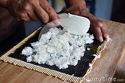 Preparing homemade sushi by putting white rice on a dried nori seaweed sheet on bamboo mat Stock Photo