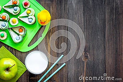 Preparing quick lunch for schoolchild. Funny sandwiches, milk, fruits on dark wooden table background top view copyspace Stock Photo