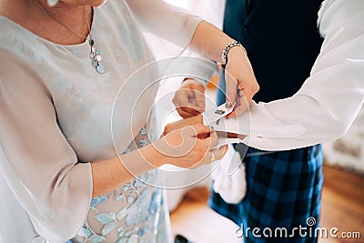 Preparing for a scottish wedding. Woman fastening cufflinks on a shirt of a man in a kilt Stock Photo