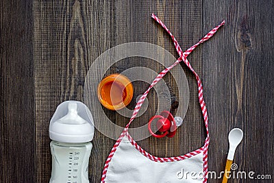 Preparing to feed baby. Puree, spoon, nipple, bottle and bib on dark wooden table background top view copyspace Stock Photo