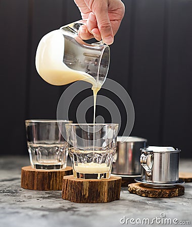 Preparing Vietnamese pour over coffee. Woman hand pouring condensed milk into glasses on dark background Stock Photo