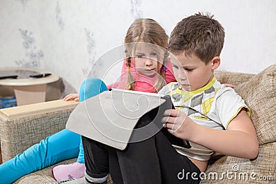 Preschool Caucasian kids having fun with pad while sitting on sofa in domestic room Stock Photo