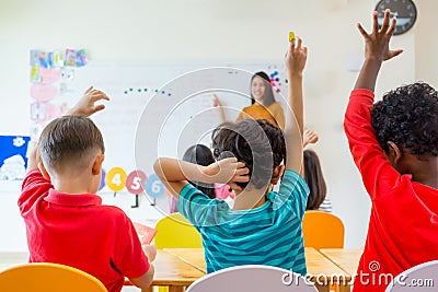 Preschool kid raise arm up to answer teacher question on whiteboard in classroom,Kindergarten education concept Stock Photo