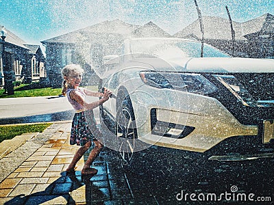 Preschool little Caucasian girl washing car on driveway in front house on sunny summer day Stock Photo