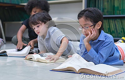 Preschool students laying on floor and rest the chin on the hand, read the book in library, Learning and education concept Stock Photo