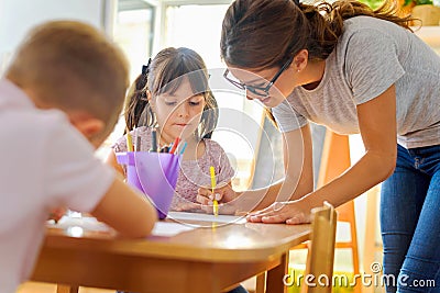 Preschool teacher looking at smart child learning to write and draw Stock Photo