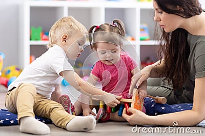 Preschooler children playing with educational wooden toys at kindergarten or day care center. Toddlers with teacher in Stock Photo