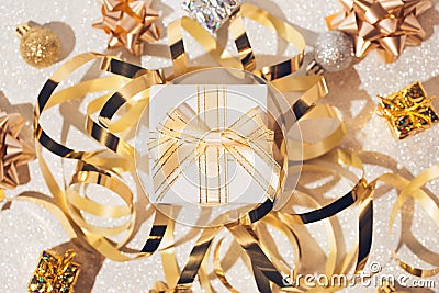 Present box, balls, golden streamer and decorative bows on white glittering background Stock Photo