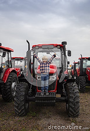 Presentation and sale of new red tractors standing in a row. The child happily stands on a farm tractor Stock Photo