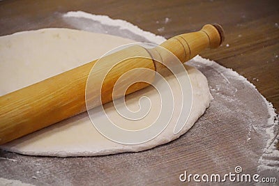 A wooden rolling pin lies on a rolled yeast dough on a wooden table in flour. Stock Photo