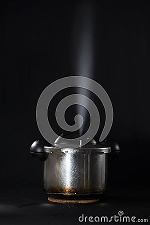 Pressure cooker releasing steam through the lid, against a black background Stock Photo