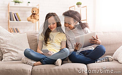 Preteen girls with gadgets sitting on sofa at home Stock Photo