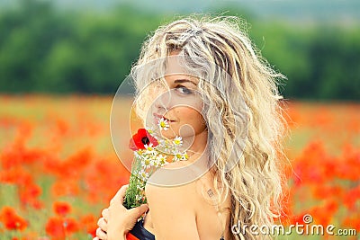 Pretty attractive lady with blond curly hair that fell on her face, in a beautiful red poppy field, turns to the camera Stock Photo