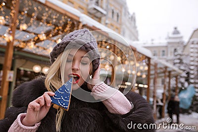 Pretty blonde girl bites tasty gingerbread cookie against light Stock Photo