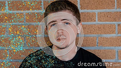 A pretty boy covered in paint leans against a brick wall Stock Photo