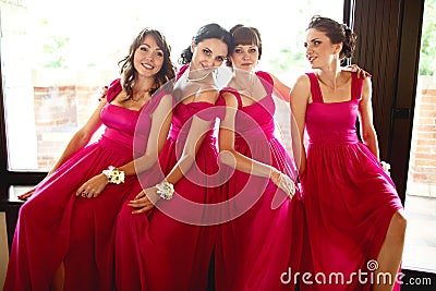 Pretty bridesmaids in pink dresses sit behind a big window Stock Photo