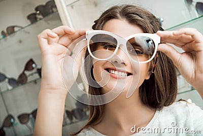 Pretty brunette girl smiling, trying on sunglasses in optical shop. Charming feminine woman in sunglasses store fooling Stock Photo