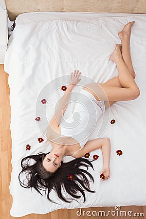 Pretty brunette posing in bed with flowers Stock Photo