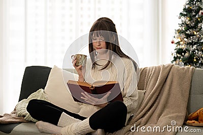 A pretty caucasian woman is reading a book and sipping coffee on a couch in her living room Stock Photo