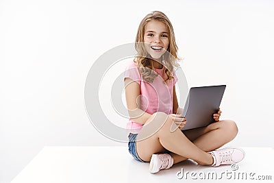 Pretty cheerful little kid girl sit crossed legs, hold laptop, studying at home, excited learn new information, studying Stock Photo
