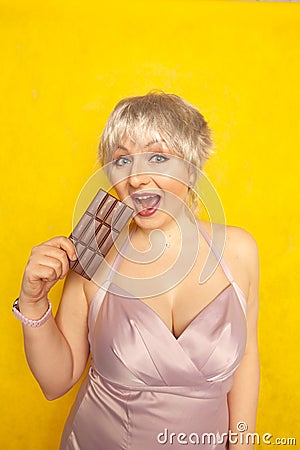 Pretty chubby girl with chocolate bar on yellow studio solid background Stock Photo