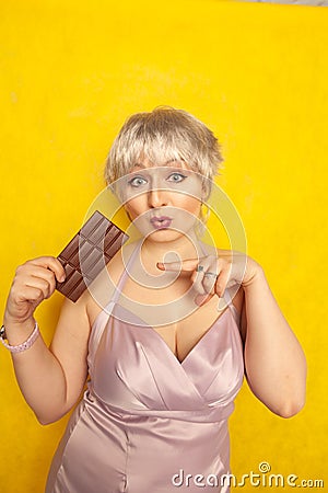 Pretty chubby girl with chocolate bar on yellow studio solid background Stock Photo