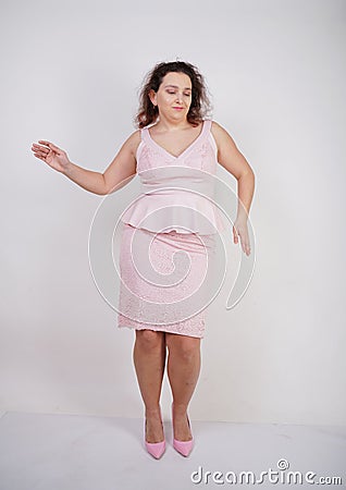 Pretty chubby positive girl dancing in pink fashionable dress on white studio background Stock Photo