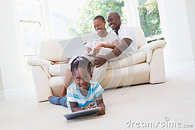 Pretty couple using laptop on couch and their daughter using tablet Stock Photo