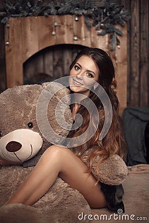 Pretty cute brunette girl posing with big teddy bear on the floor in cozy comfortable interior home. Stock Photo