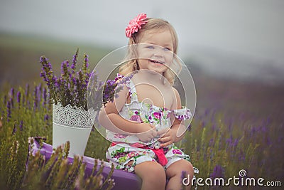 Pretty cute little girl is wearing white dress in a lavender field holding a basket full of purple flowers Stock Photo