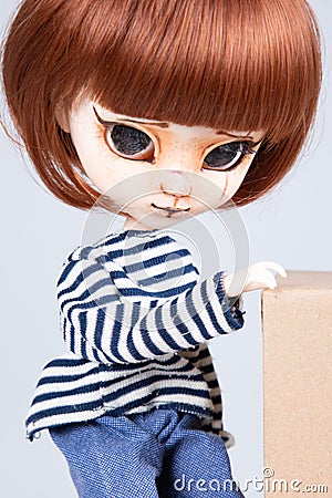 Pretty expressive doll with big eyes red hairs in blue shirt hand on carton box in white background Stock Photo