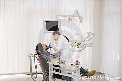 Pretty female asian dentist in white uniform, making dental check up and caries treatment with drill Stock Photo