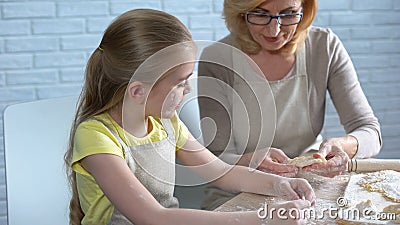 Pretty female preschooler trying to cook pastry, helping her granny in kitchen Stock Photo