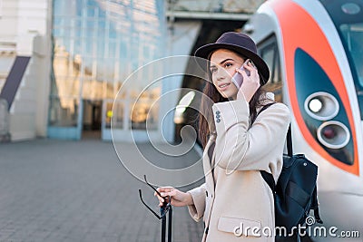 Pretty female tourist talking on the phone while standing on the platform against the background of the train. Stock Photo