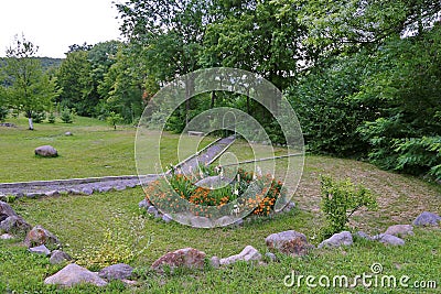 A pretty flowerbed on a green lawn with a lying stone in the middle of it and growing flowers around in a park area next Stock Photo