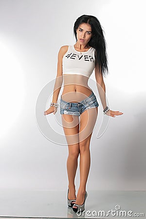 A pretty girl brunette stretching instructor, go-go, trainer, danser, posing in the studio on a white background in shorts and T- Stock Photo