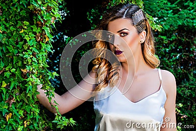Pretty girl with golden hair posing in the garden next to ivy Stock Photo