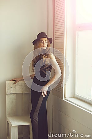 Pretty girl in hat and dress at chair and window Stock Photo