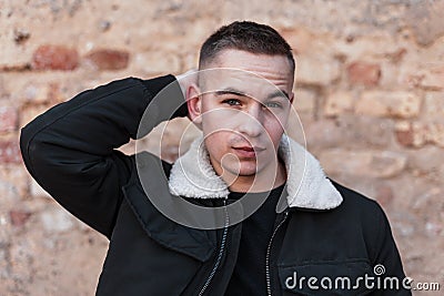 Pretty handsome attractive young man in a trendy black jacket in a stylish t-shirt with a fashionable hairstyle stands Stock Photo